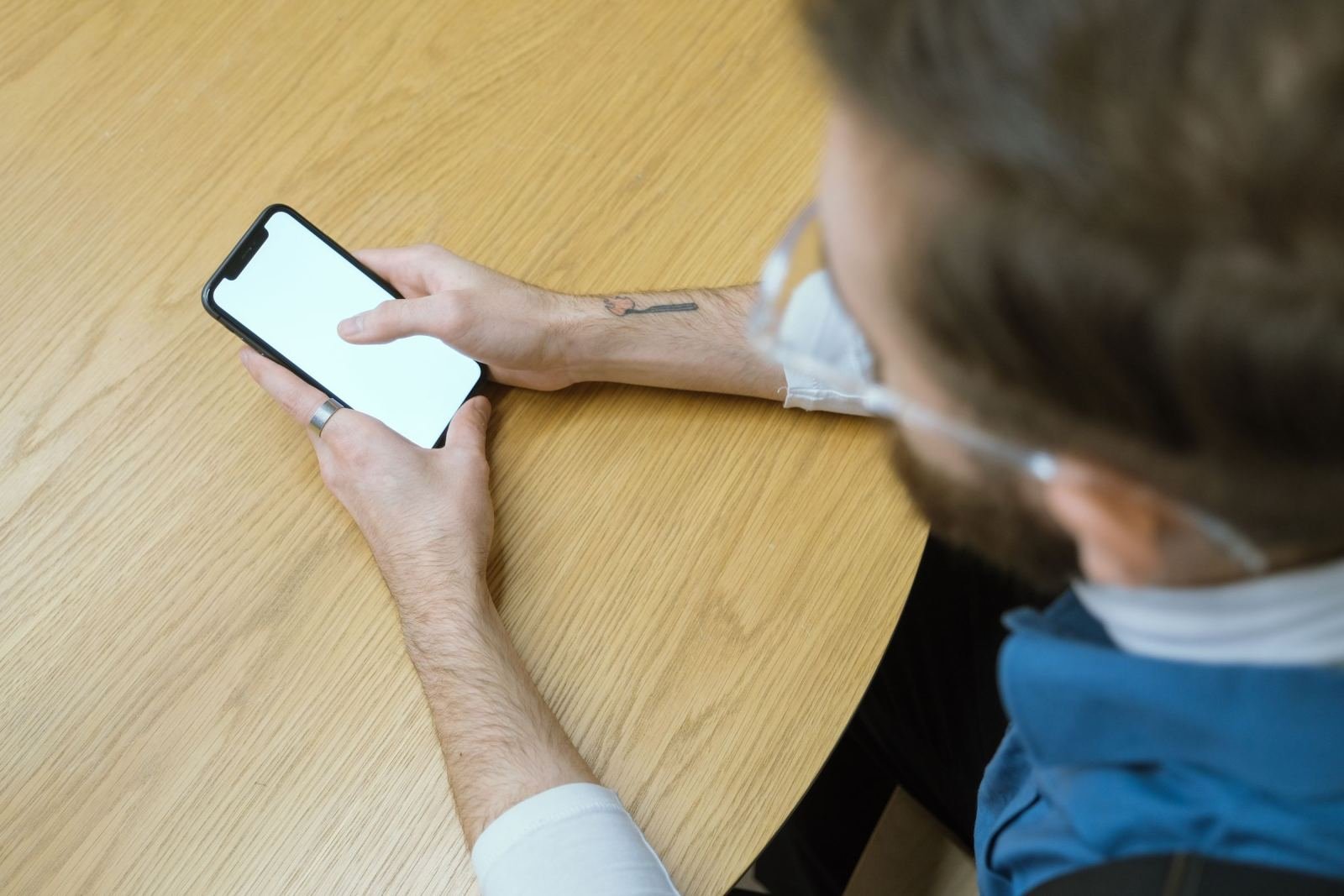 A man uses a smartphone while sitting at a wooden table