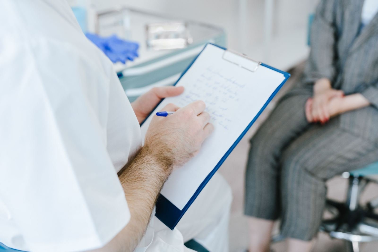 A healthcare provider in a white coat writes on a clipboard while meeting with a patient