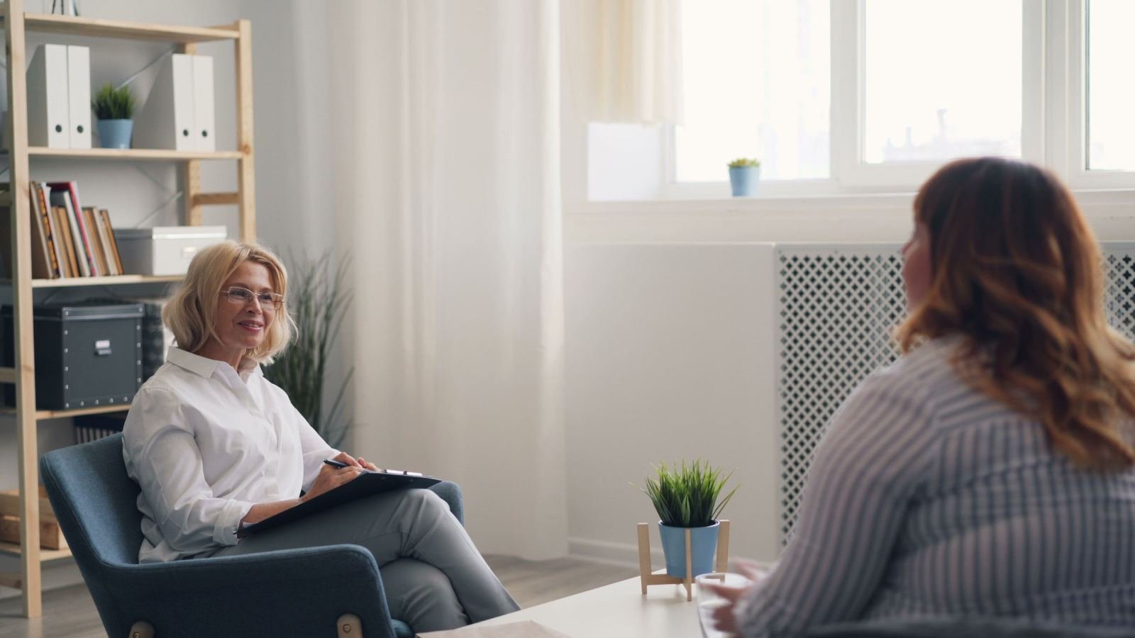 A counselor with a clipboard talks with a client in a bright office