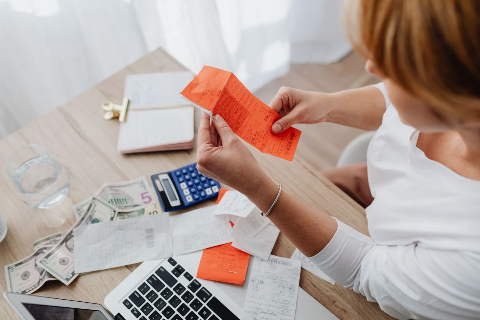 A person reviews orange receipts and bills at a table with a laptop and calculator