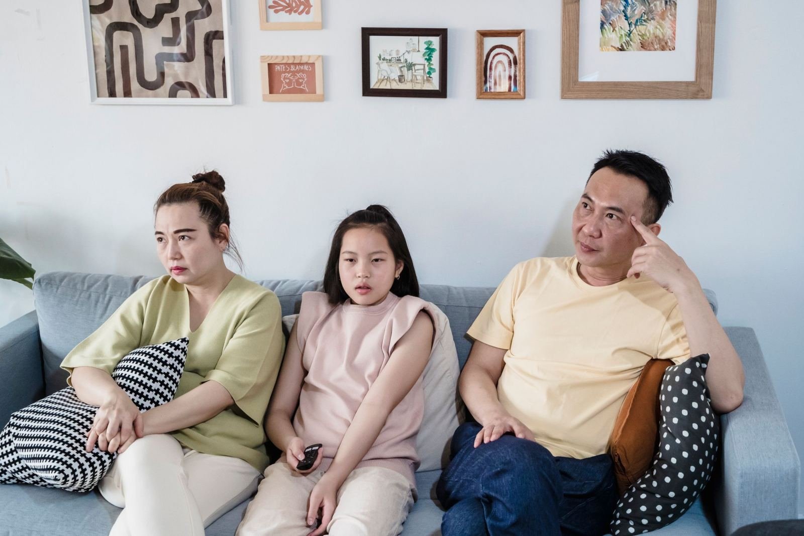 A woman, a young girl, and a man sit on a sofa with concerned expressions