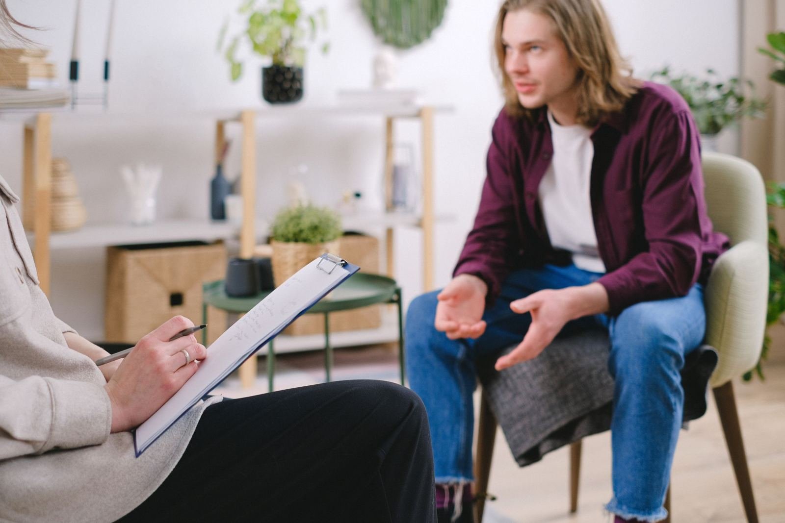 A counselor with a clipboard listens to a man in a purple shirt in a bright office