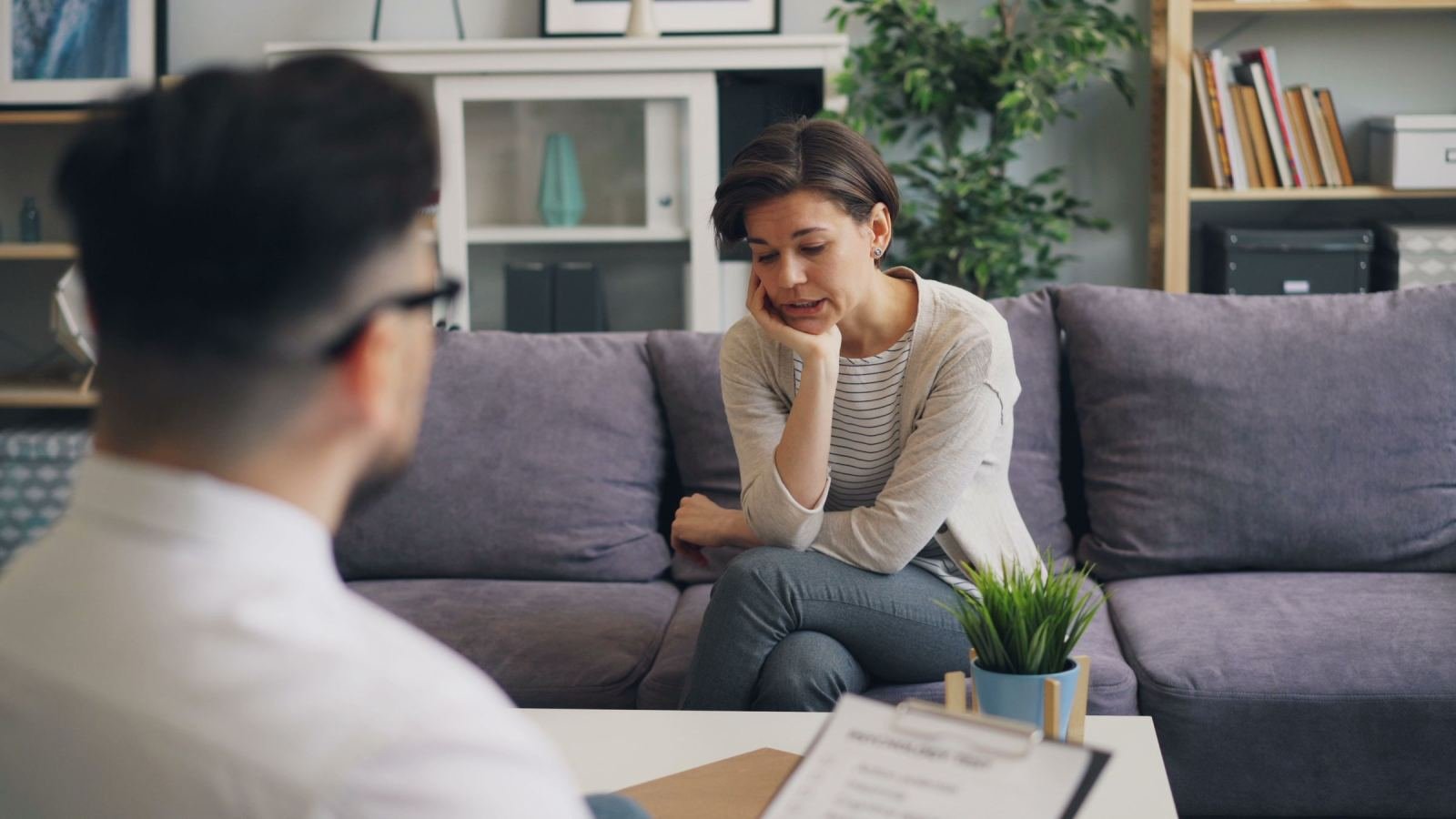 A woman sits on a sofa talking to a clinician in a quiet office