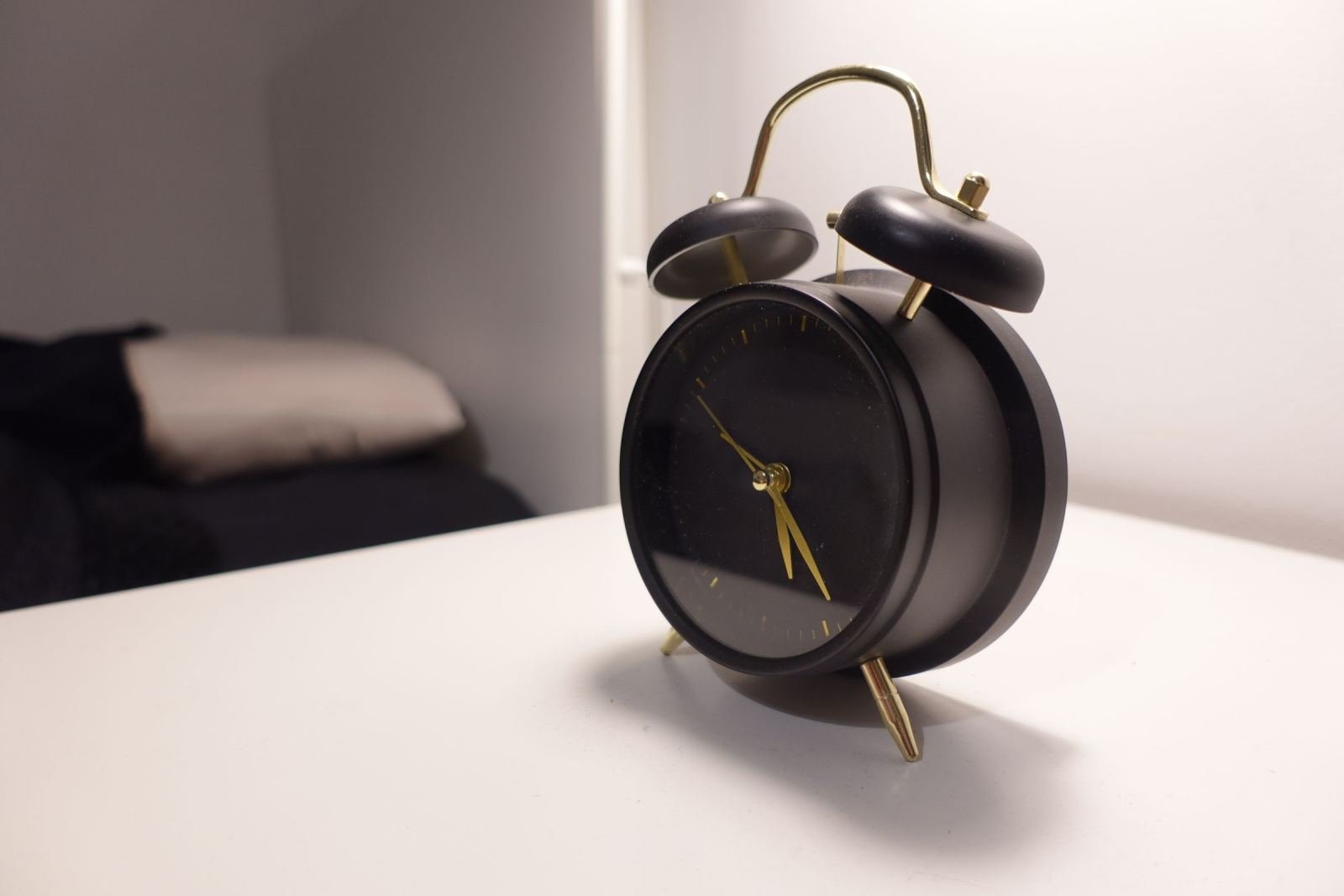 A black alarm clock with gold hands and bells on a white nightstand