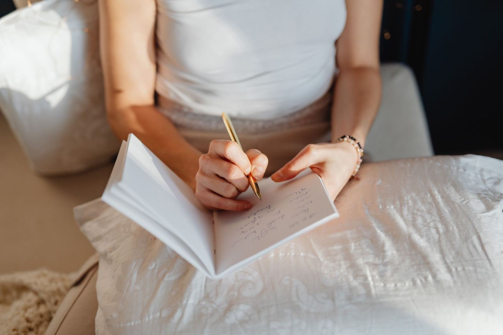 A person writing notes in a white journal with a gold pen