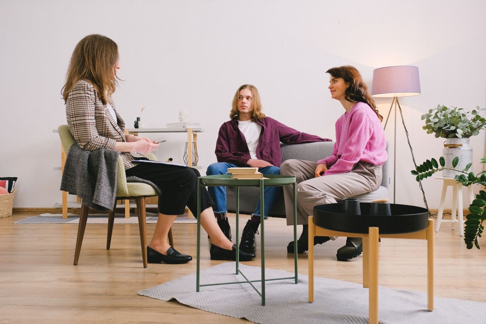 A woman in a blazer talks with a man and a woman sitting on a sofa