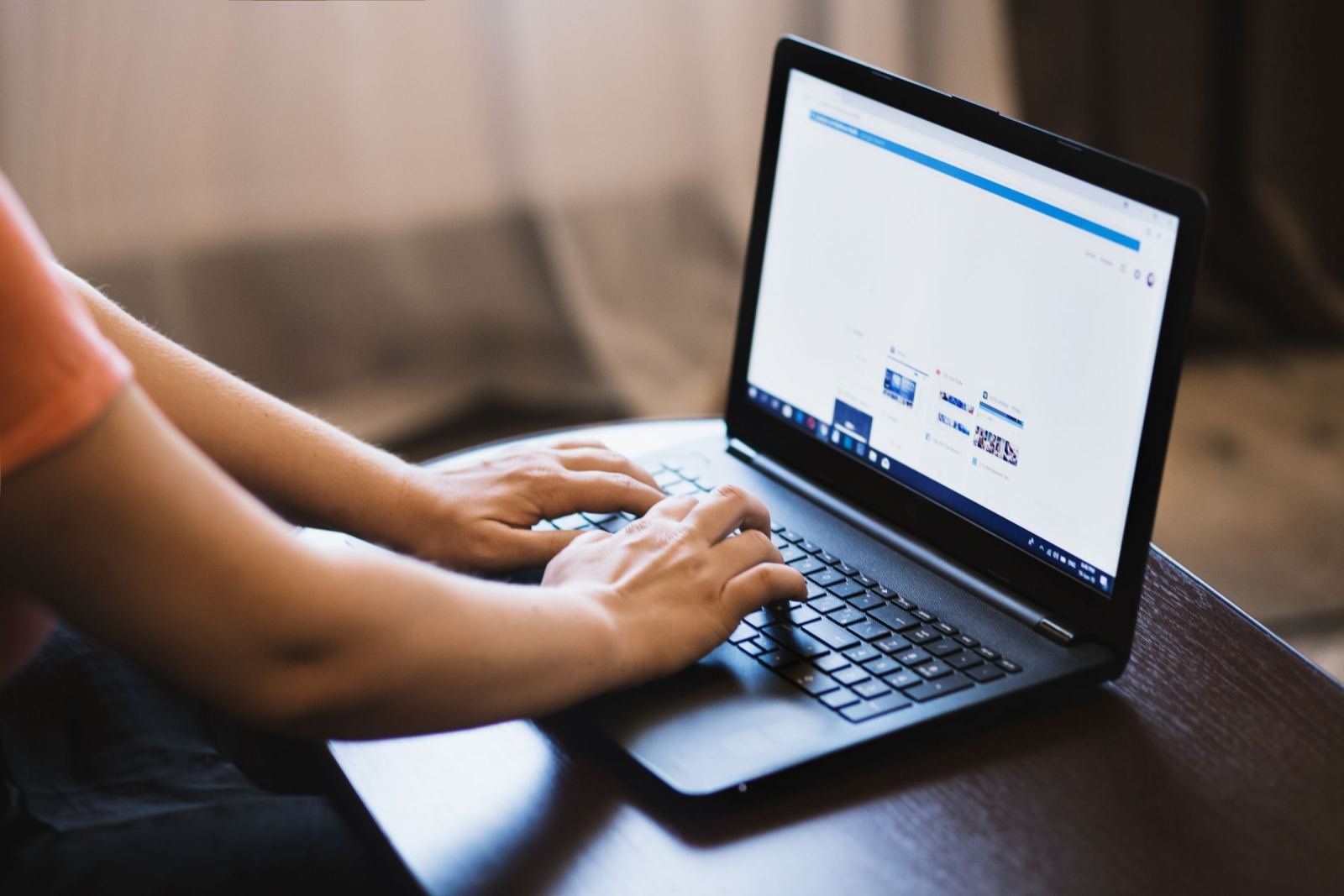 A person's hands typing on a laptop at a wooden desk