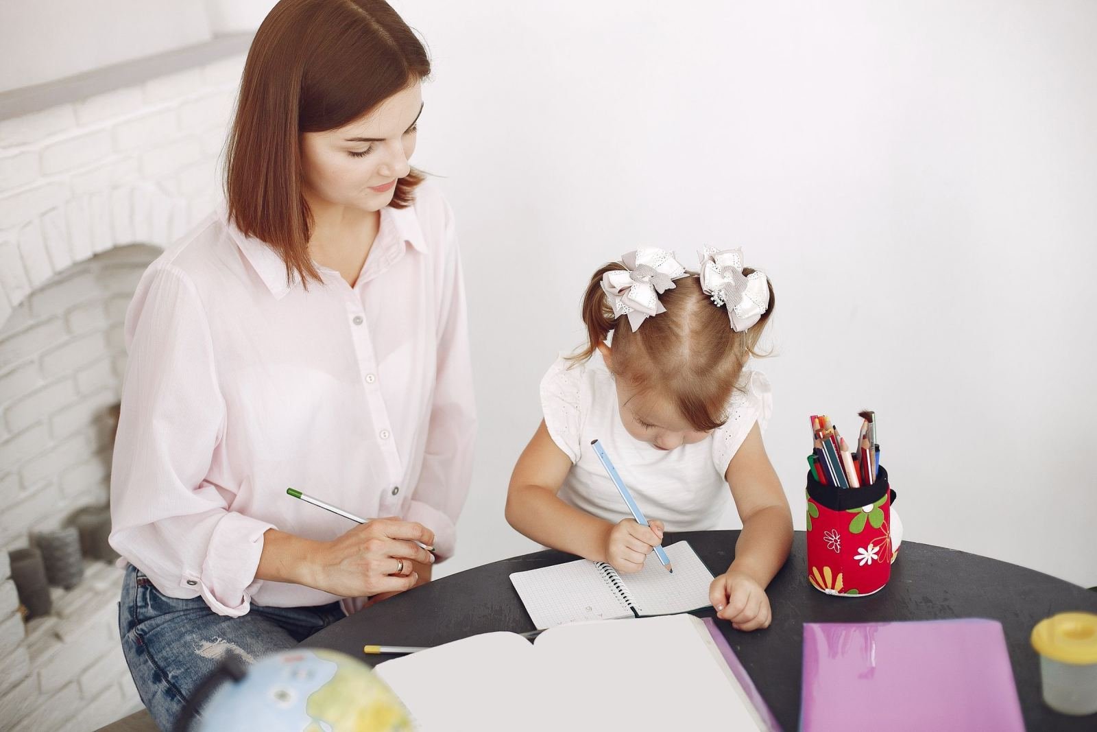 A woman and a young girl write in a notebook together at a table