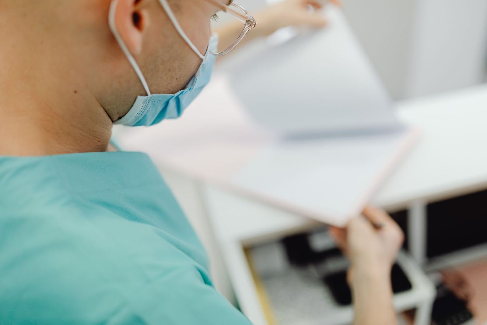 A clinician in scrubs and a mask reviews a medical record folder