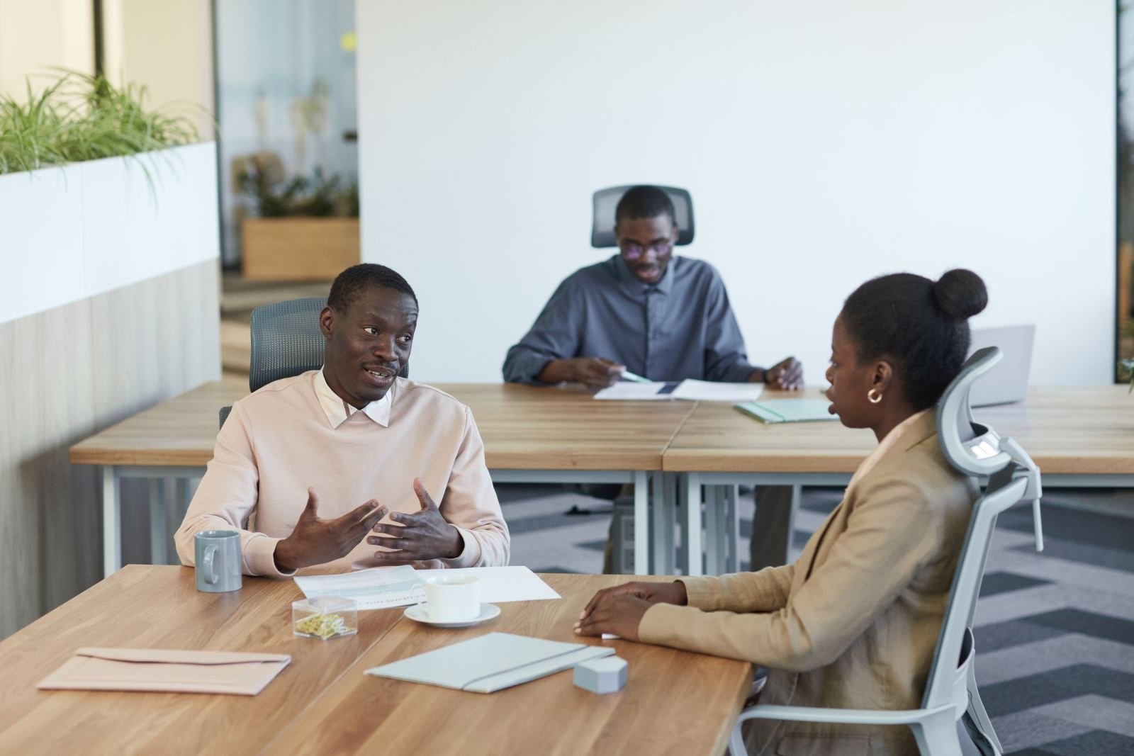 A man gestures while speaking with a woman at a wooden table in a bright office