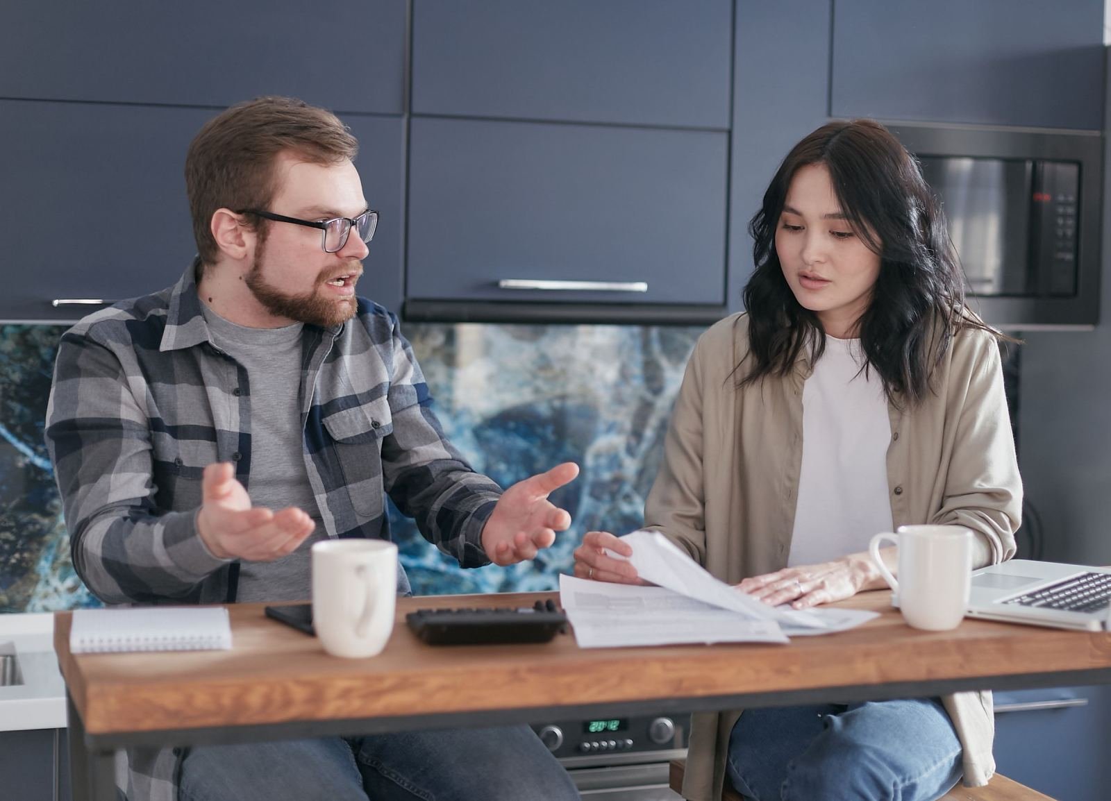 A man and woman review documents and use a calculator at a wooden table