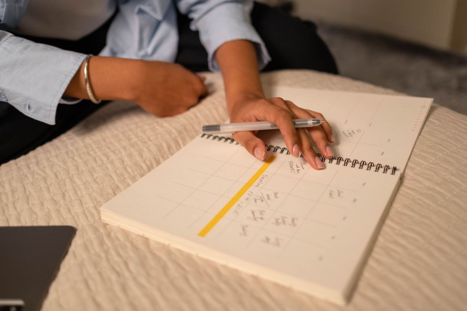 A person's hand rests on a spiral-bound calendar and notebook