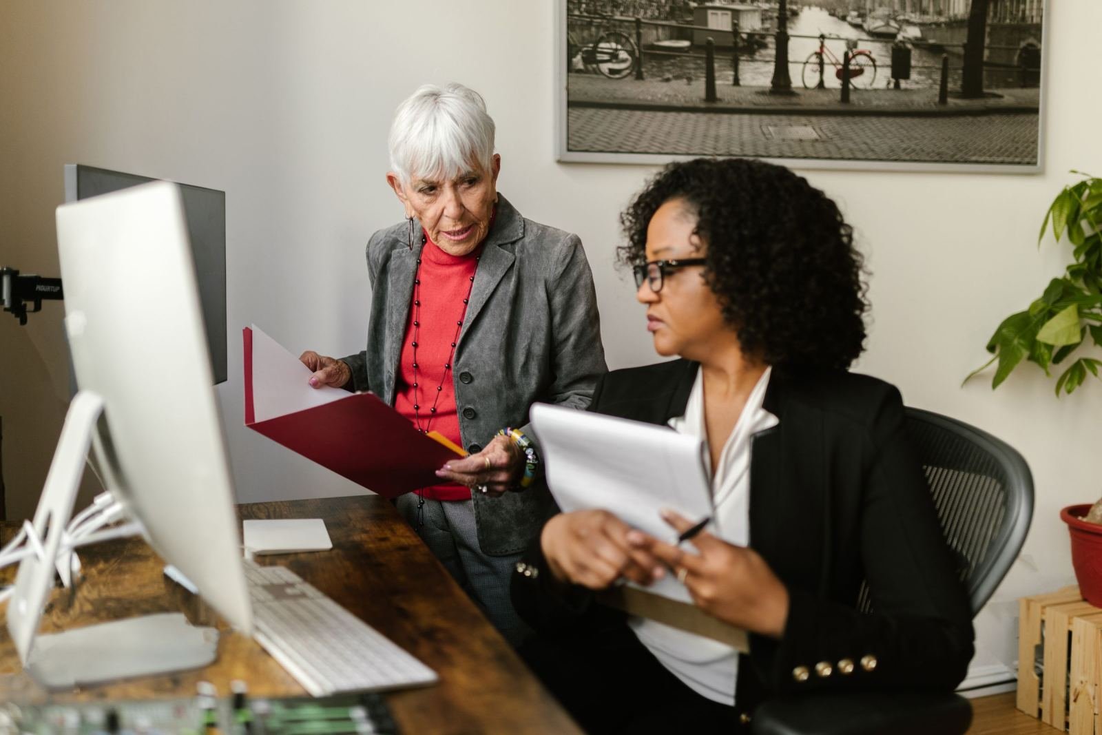 Two women in professional attire look at a computer screen together in an office