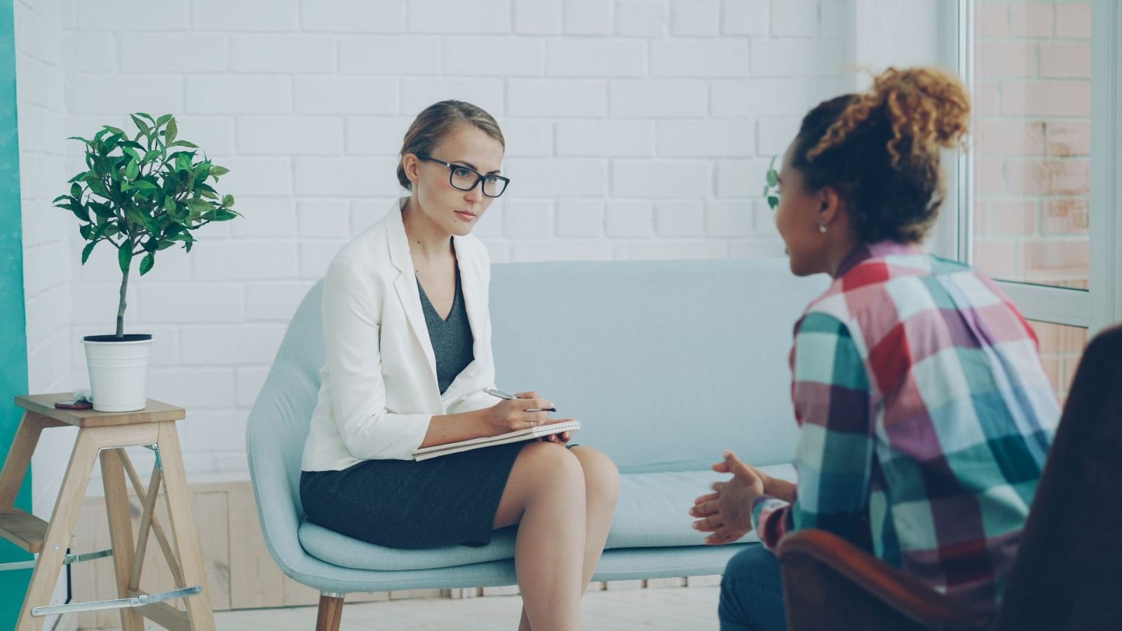 A counselor with a notebook listens to a woman in a plaid shirt