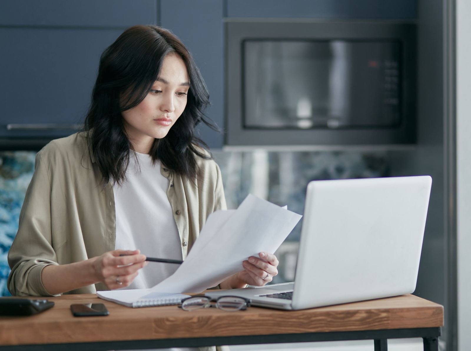 A woman reviews papers while sitting at a table with a laptop