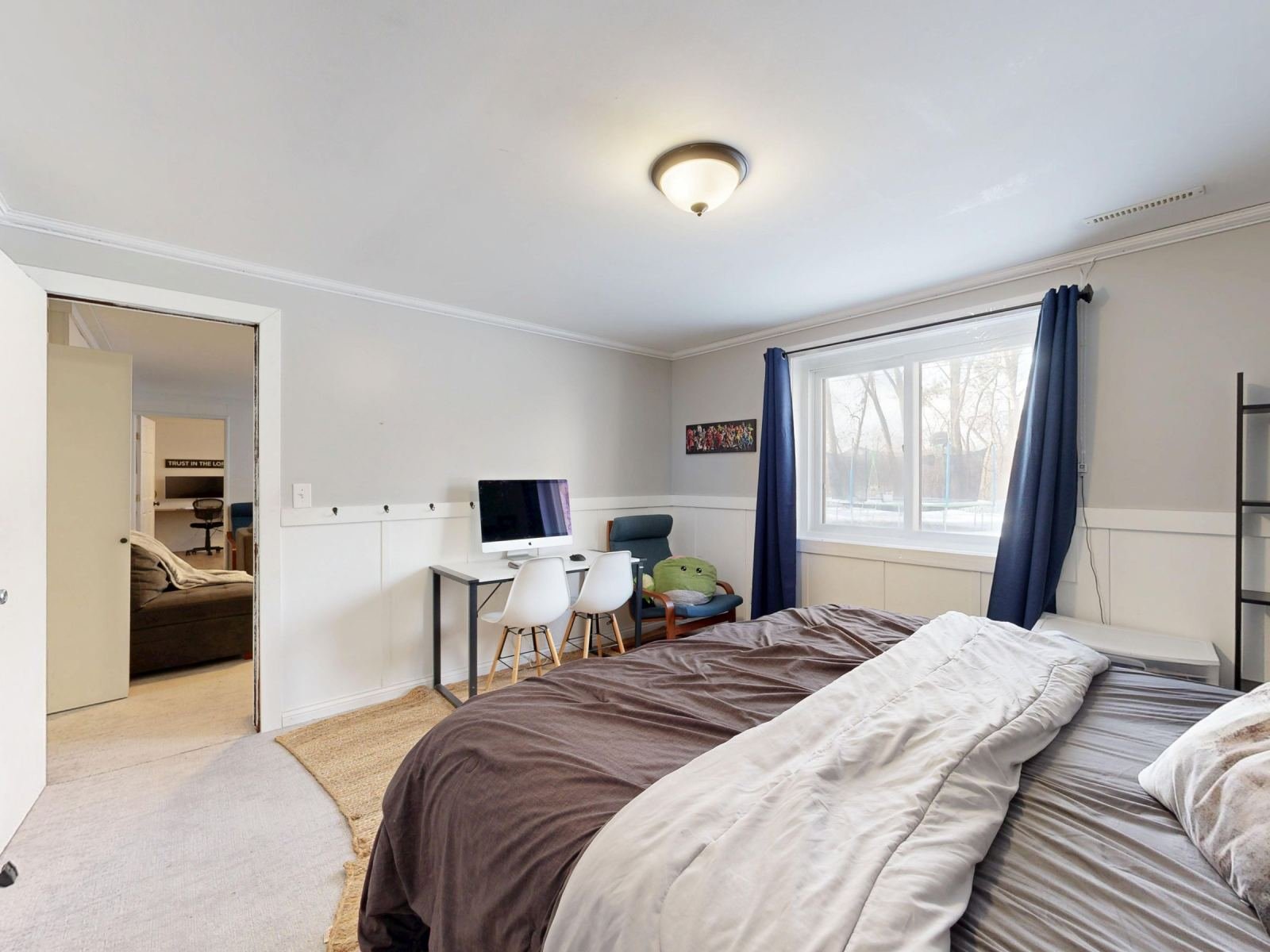 A bright bedroom with a bed, a desk with a computer, and blue curtains