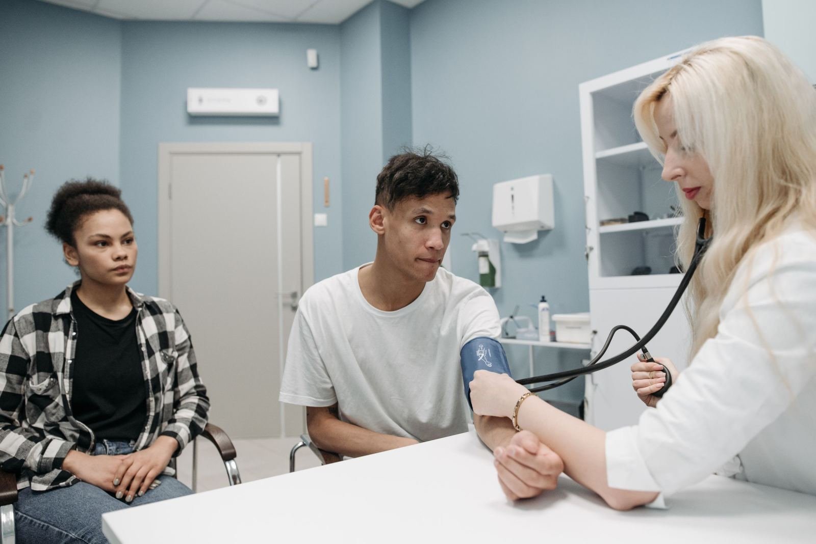 A healthcare provider takes a man's blood pressure while a woman looks on