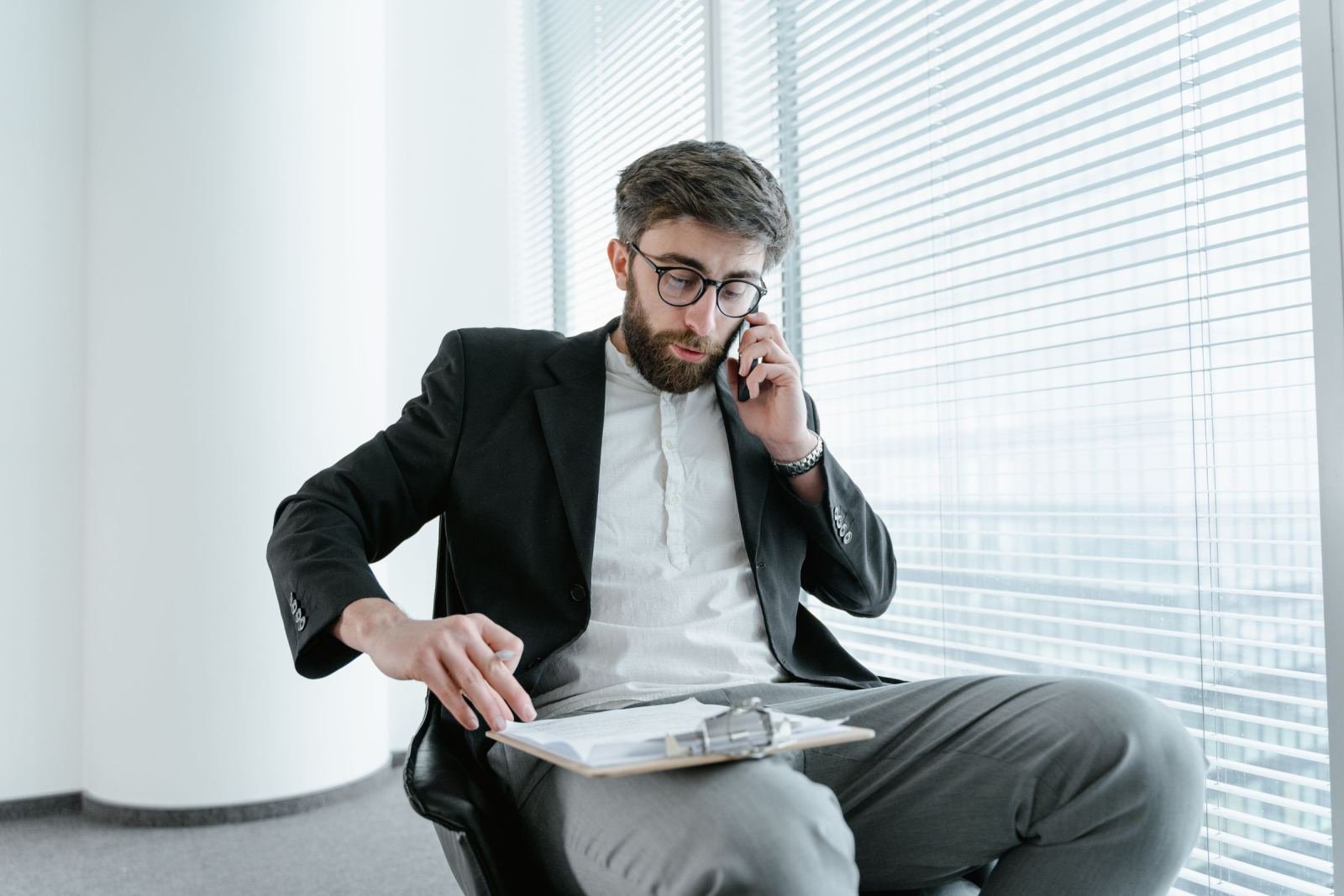 A man in a blazer talks on a mobile phone while holding a clipboard