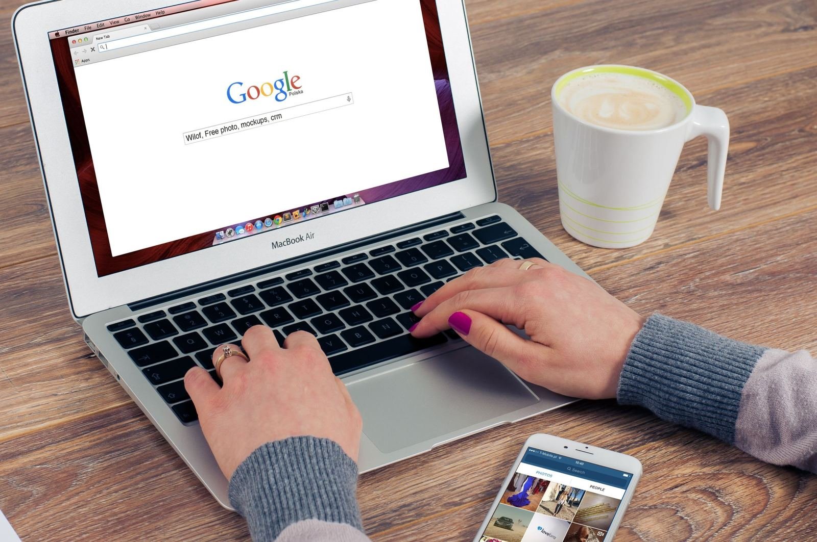 Hands typing on a laptop next to a coffee mug and a smartphone