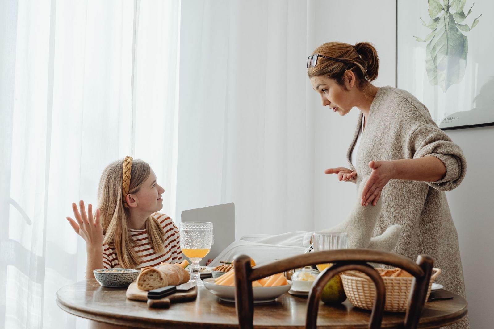 A woman gestures while talking to a young girl sitting at a dining table