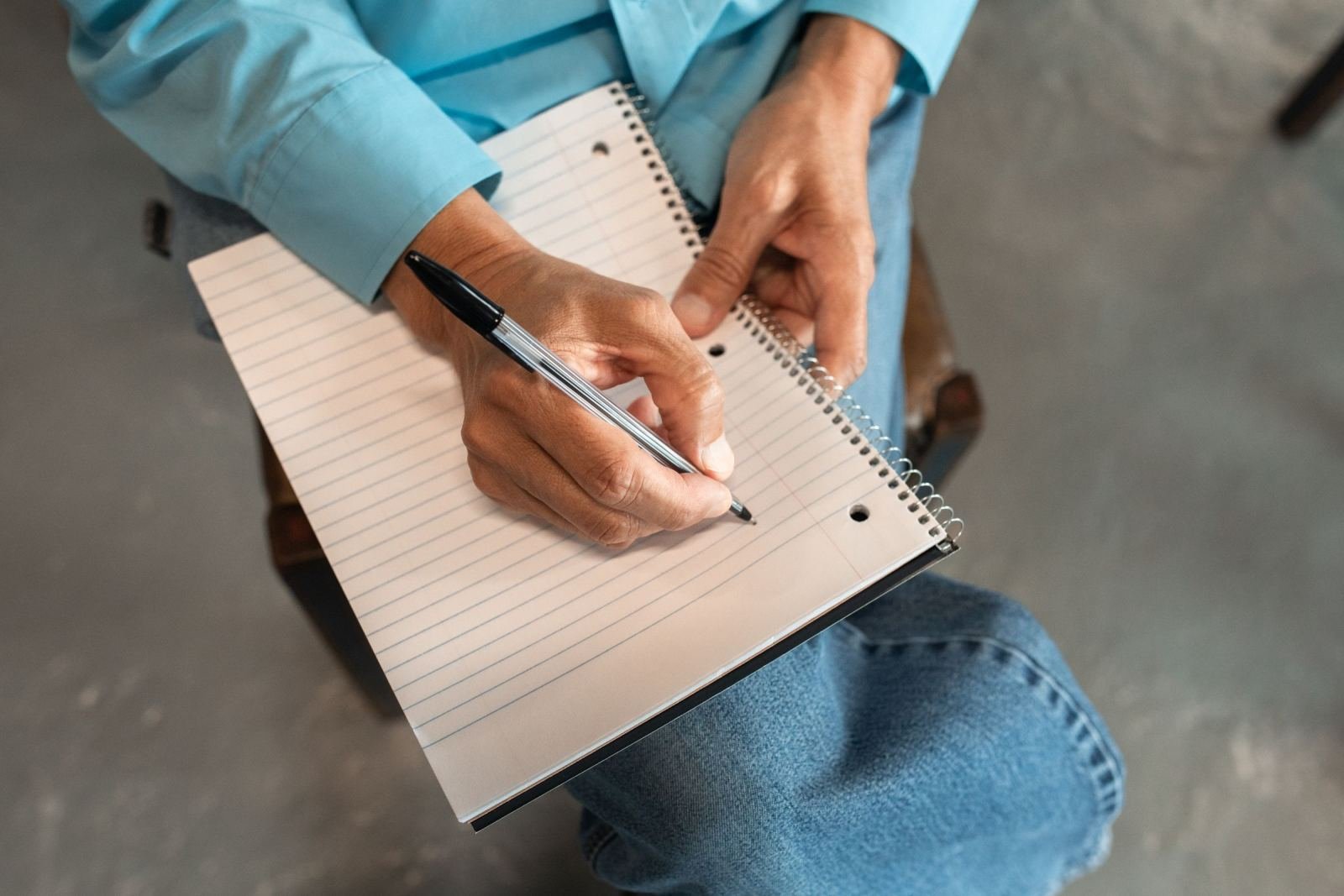 A person in a blue shirt writes in a spiral notebook
