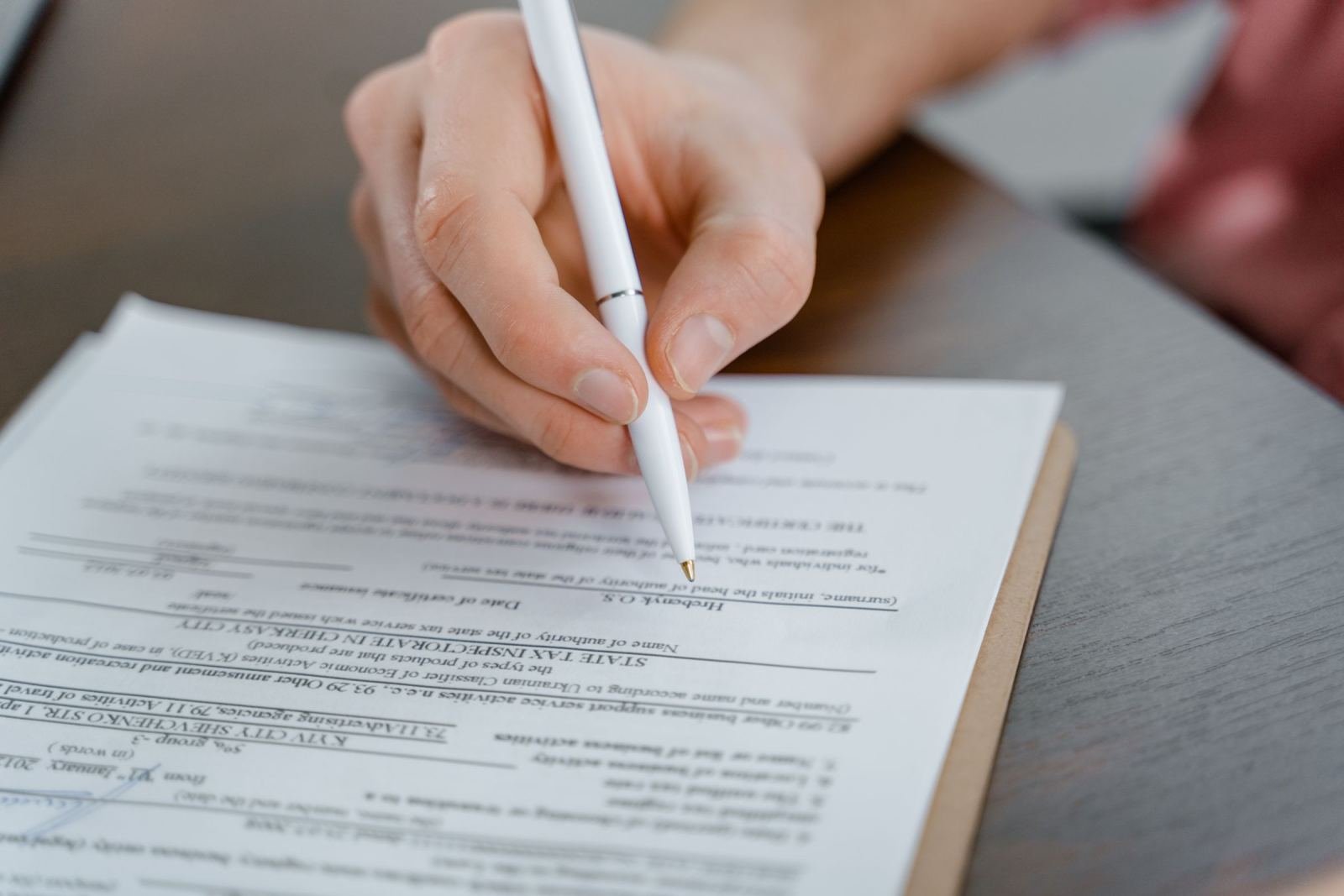 A person's hand holding a white pen over a printed form on a clipboard
