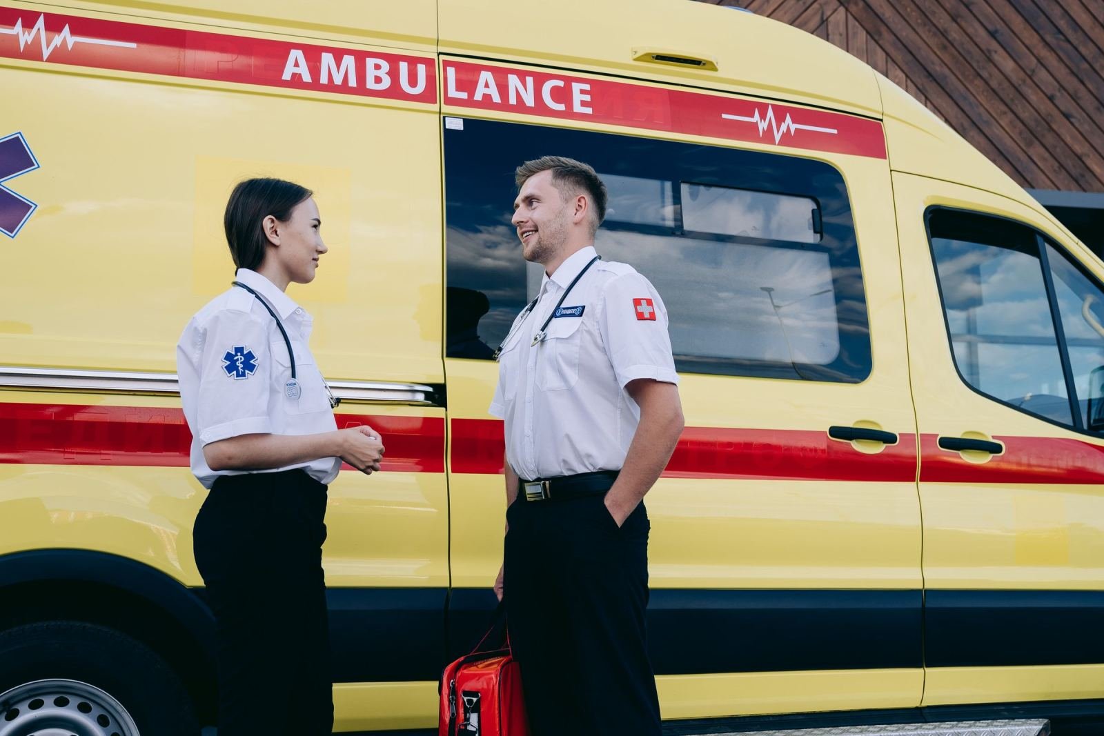 Two paramedics in uniform talking beside a yellow ambulance