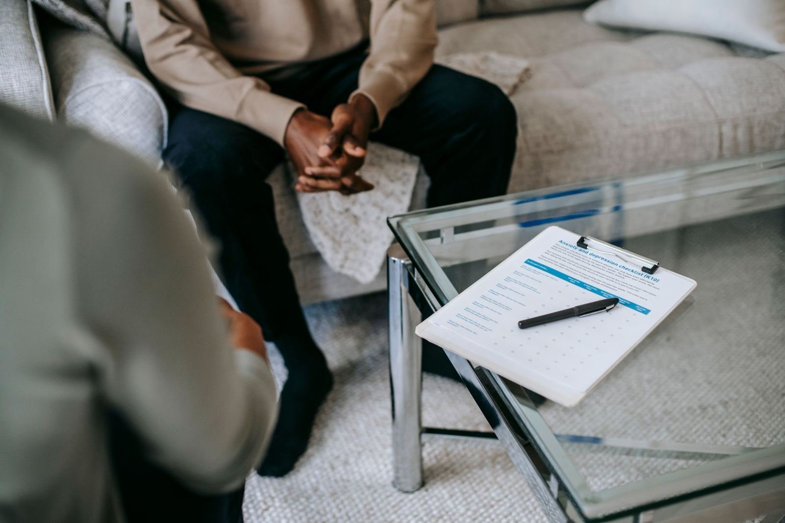 Two people sit at a glass table. Between them lies a clipboard holding a checklist, alongside a pen.