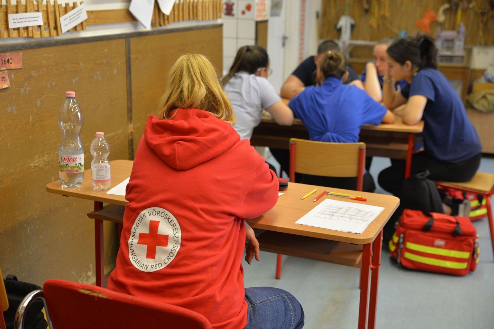 Students sit at desks in a classroom. One wears a Red Cross hoodie.