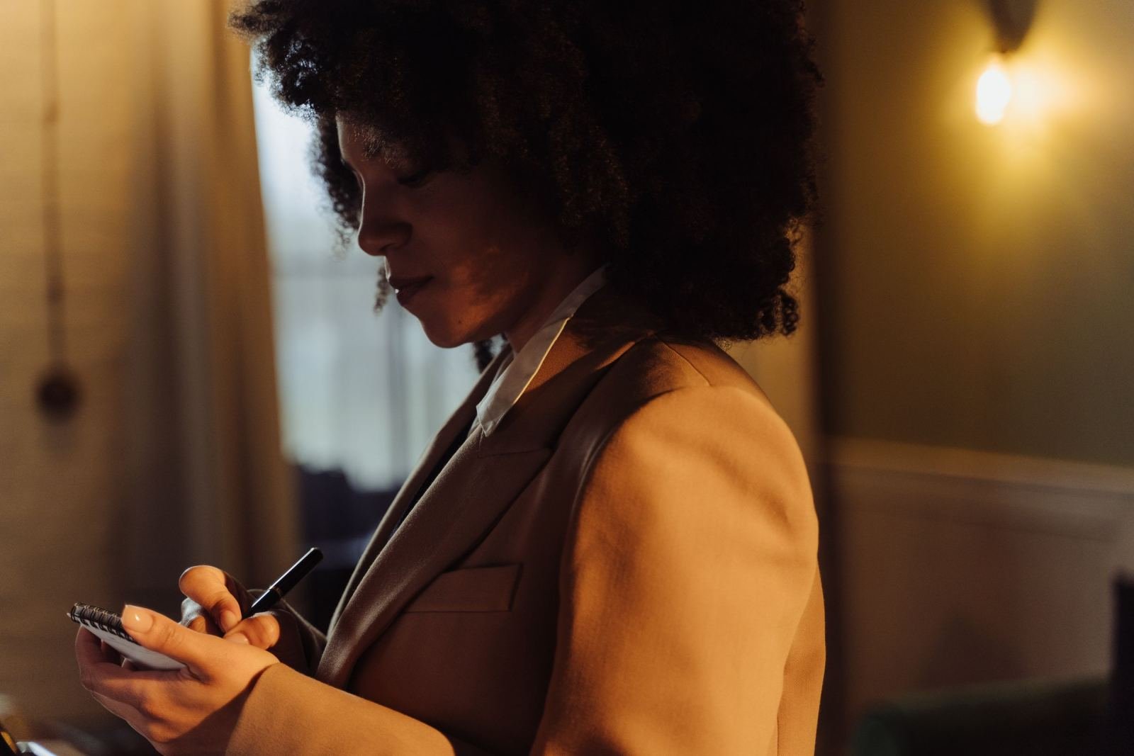 A woman in a tan blazer writes in a spiral notebook