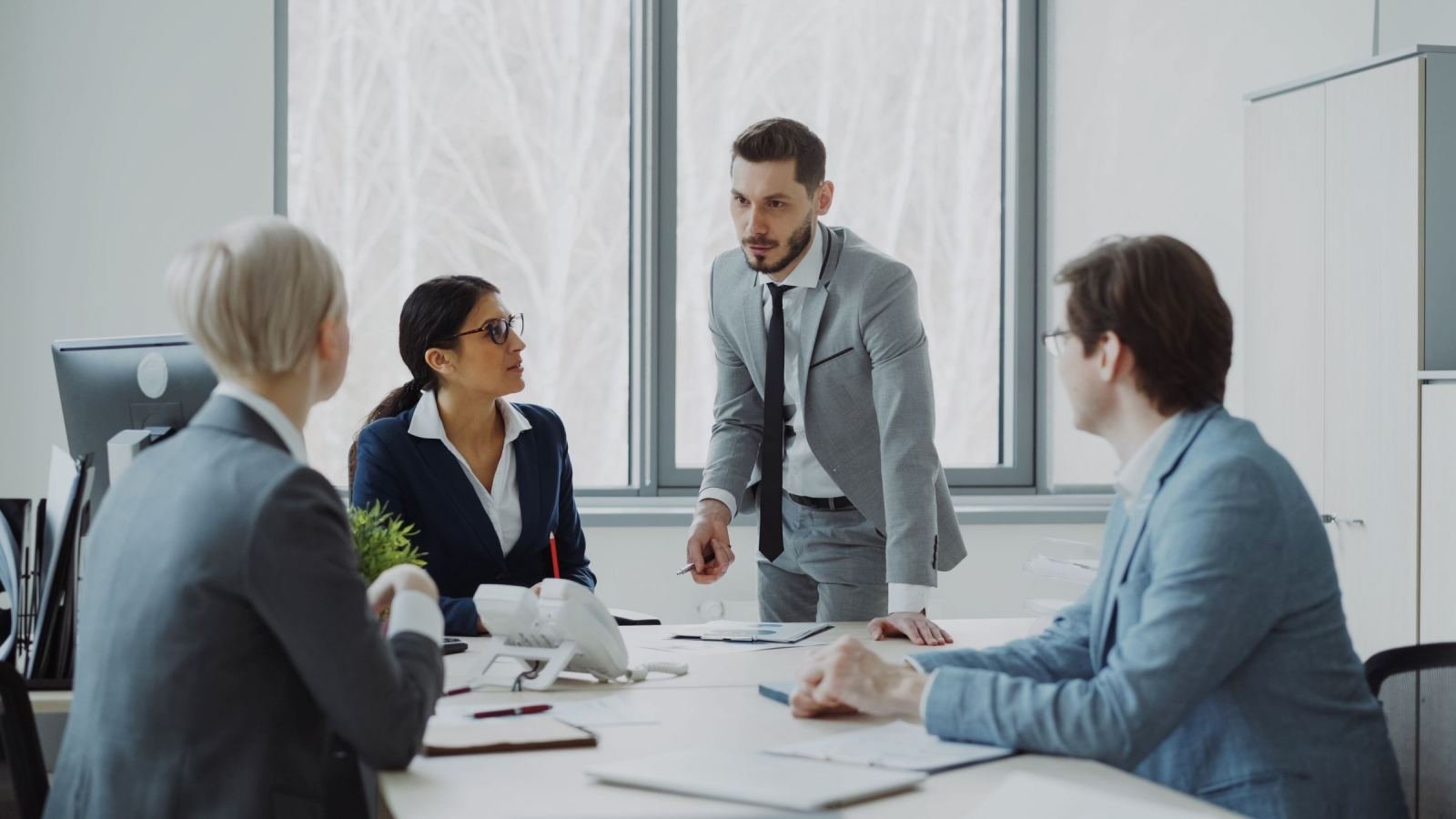 Four professionals in business attire meeting around a table in a bright office