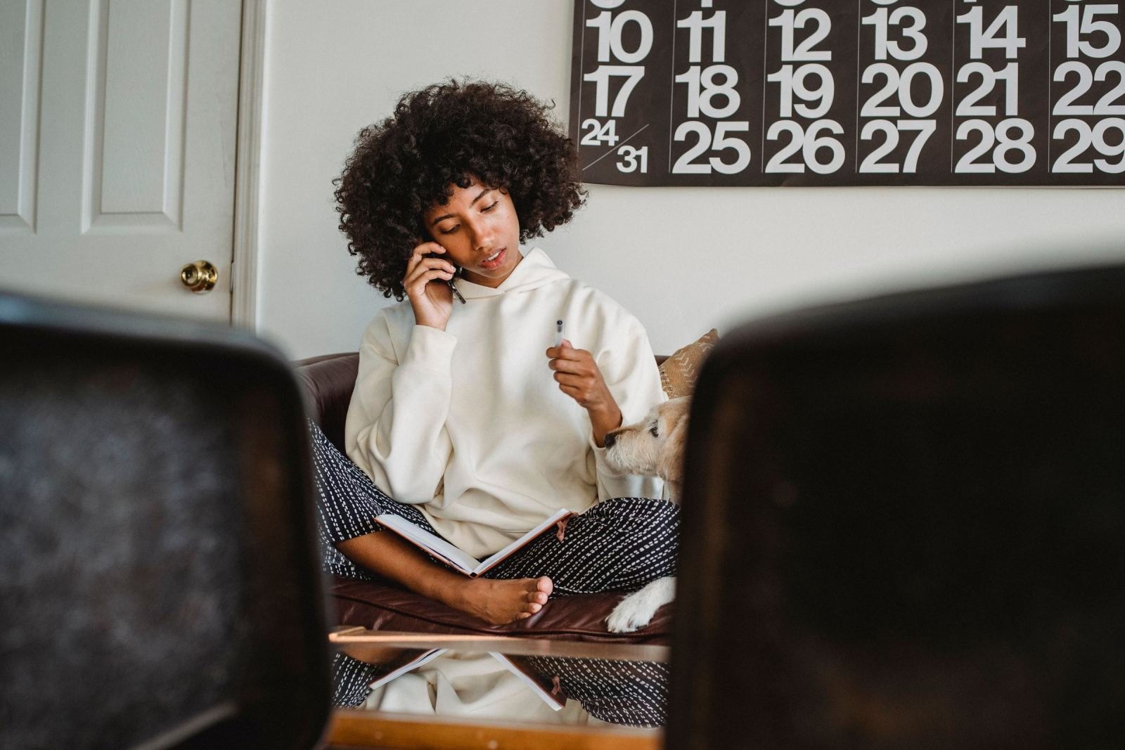 A woman talks on the phone while holding a pen with a notebook on her lap