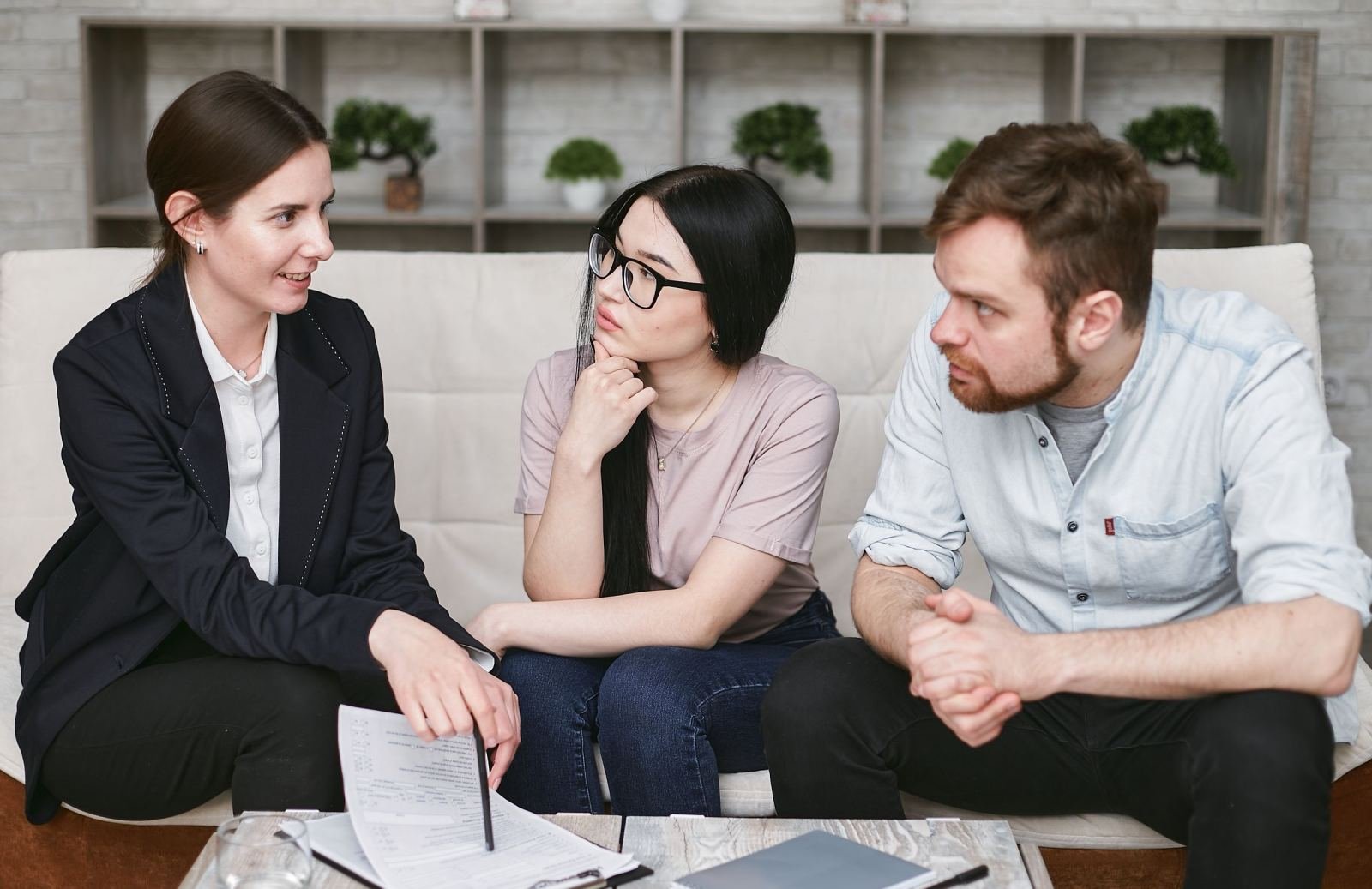 A professional woman explains a document to a couple sitting on a white sofa