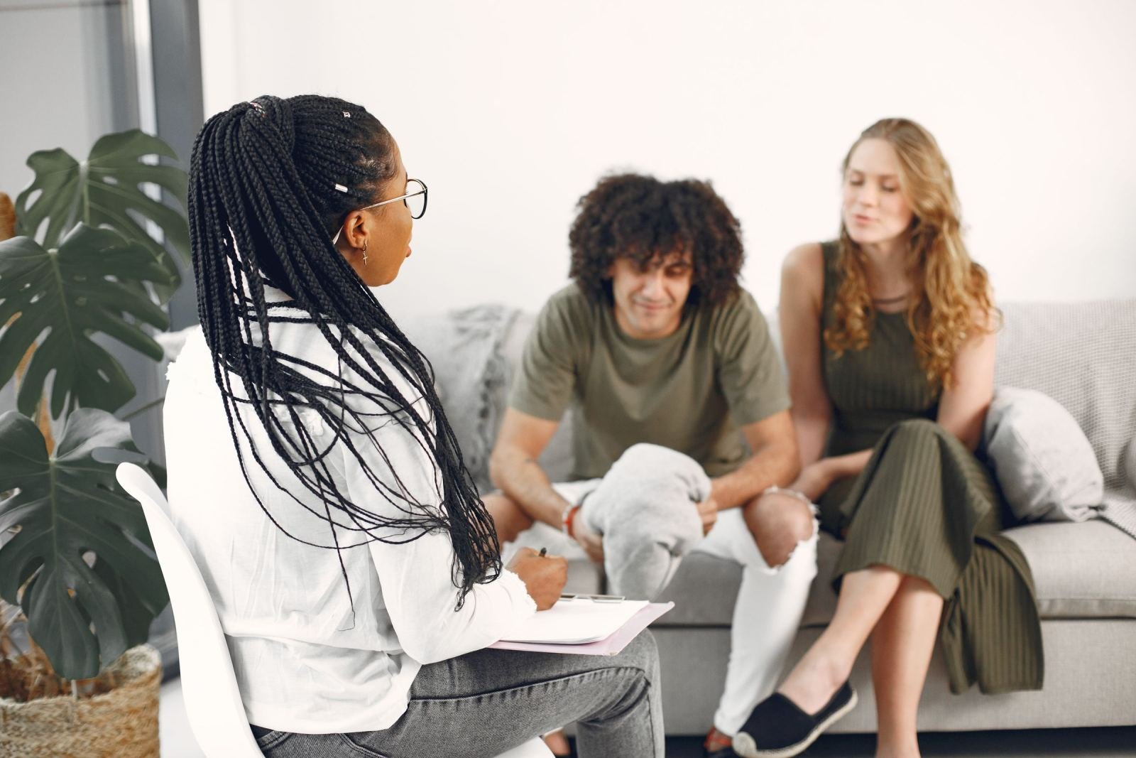 A counselor holding a clipboard speaks with a man and woman seated on a couch