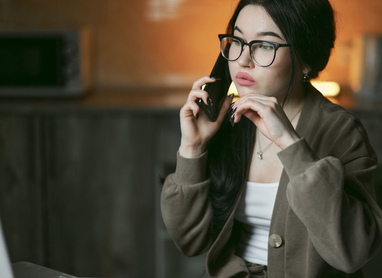 A woman with glasses talks on a phone in a dimly lit room
