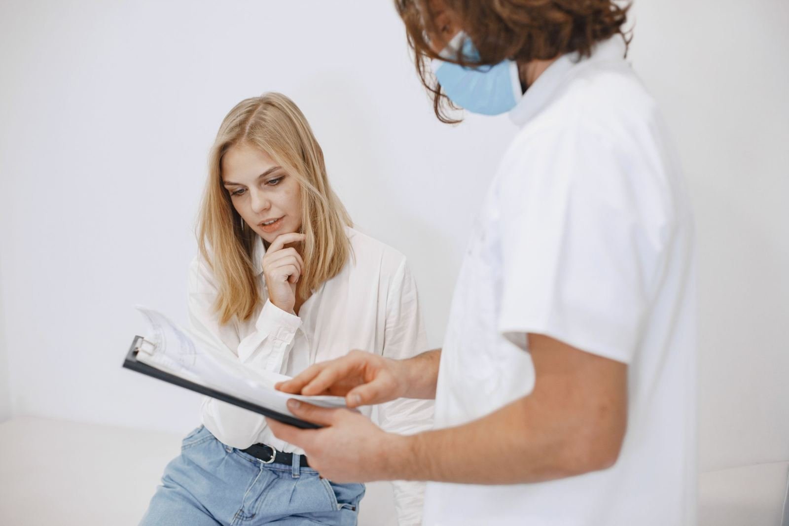 A medical professional in a mask shows a clipboard to a seated woman