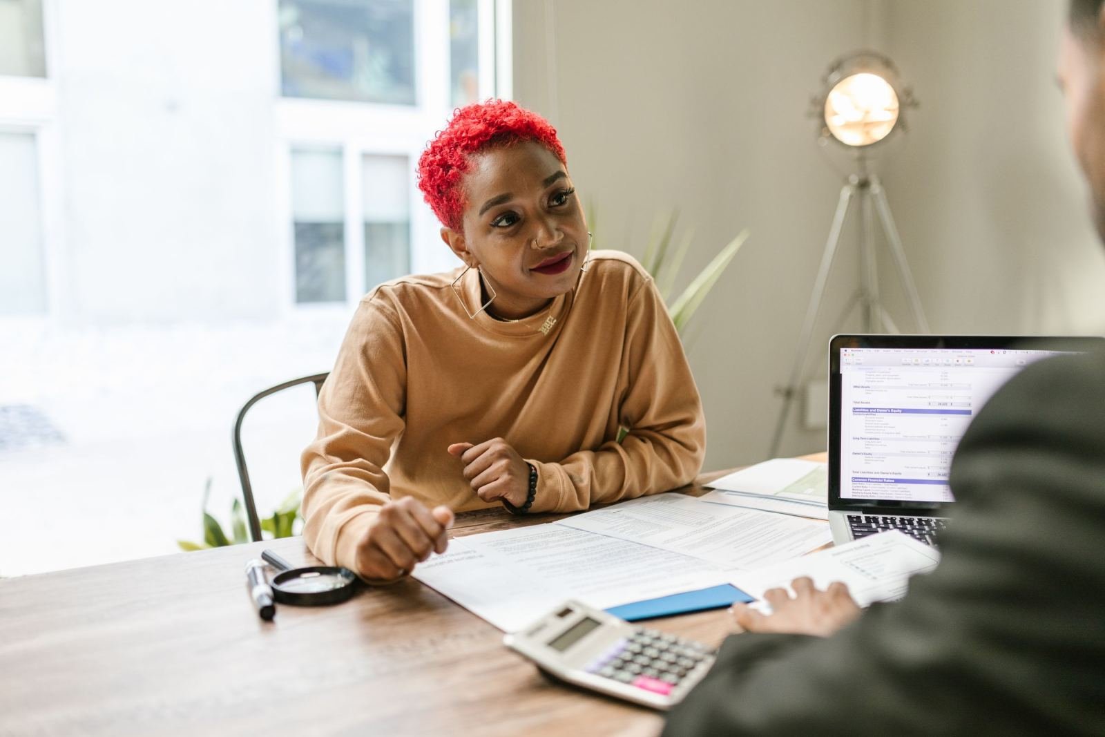 A woman with red hair speaks with an advisor across a desk with a laptop and documents