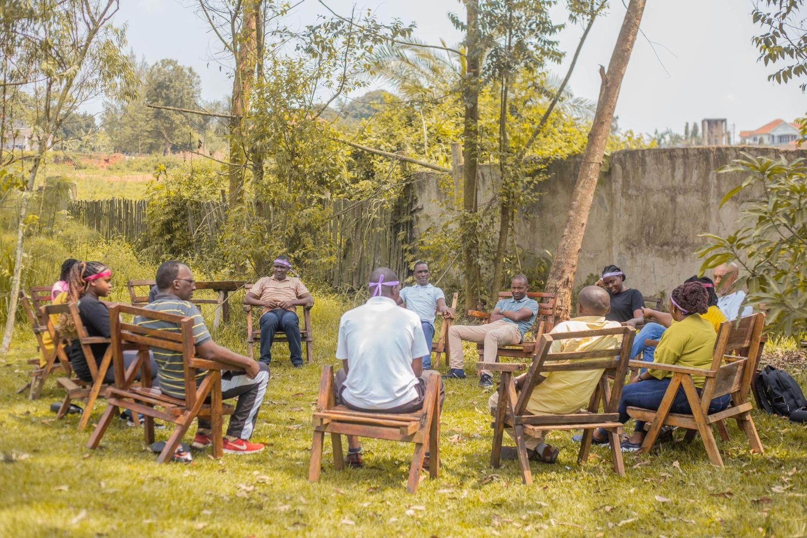 A group of people sitting in a circle of wooden chairs on a lawn
