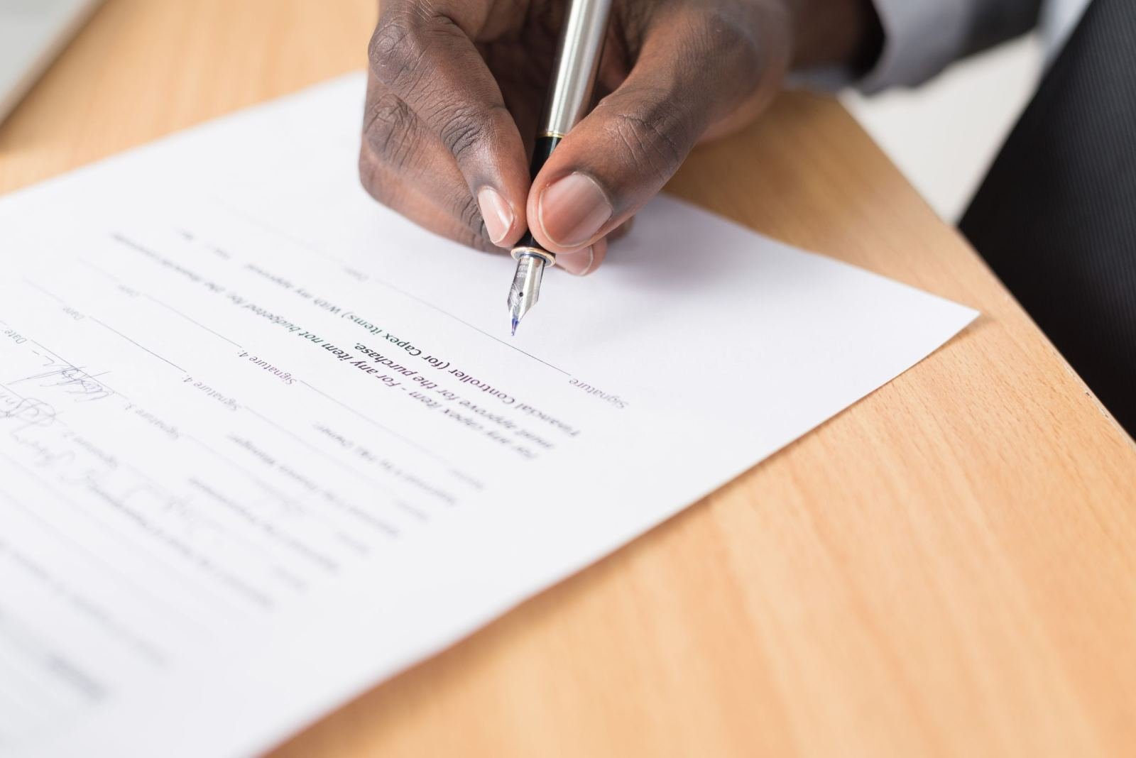 A person signing a document with a pen on a wooden desk
