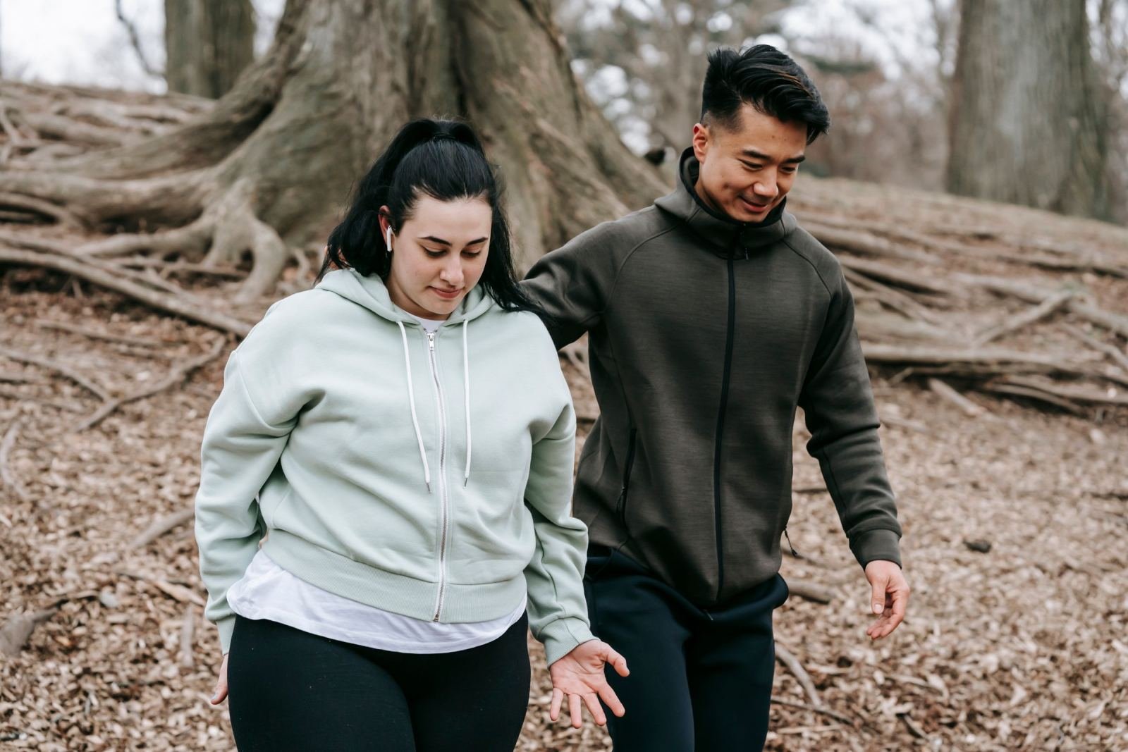 A man and woman walk together on a leaf-covered path in the woods