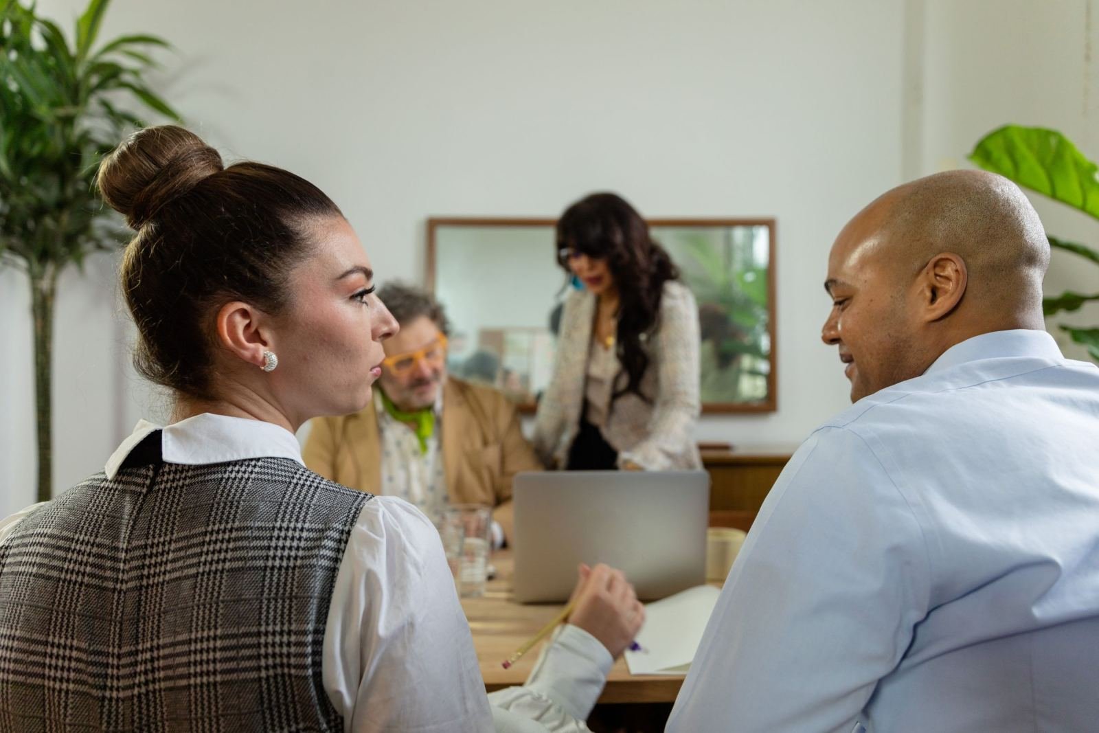 A bright office scene shows three people seated at a table with a laptop.
