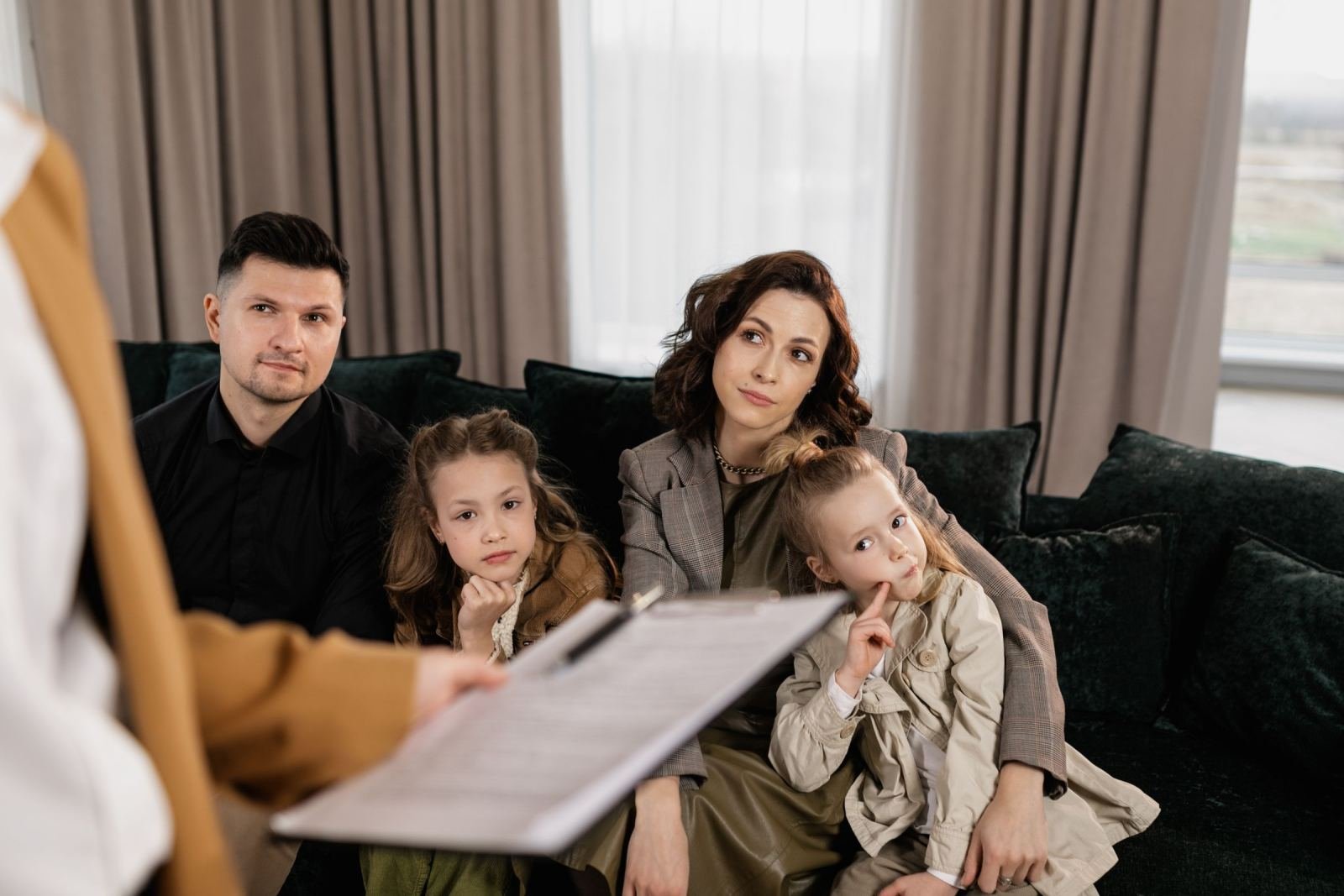 A family of four looks at a document on a clipboard while sitting on a green couch