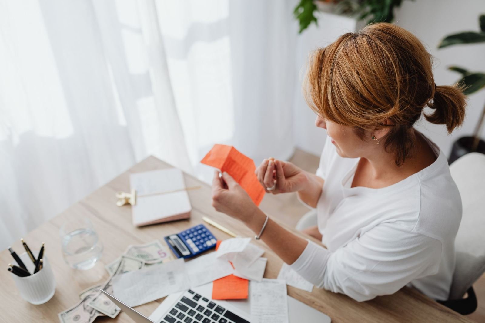 A woman sorts through mail and bills at a table with a laptop and calculator