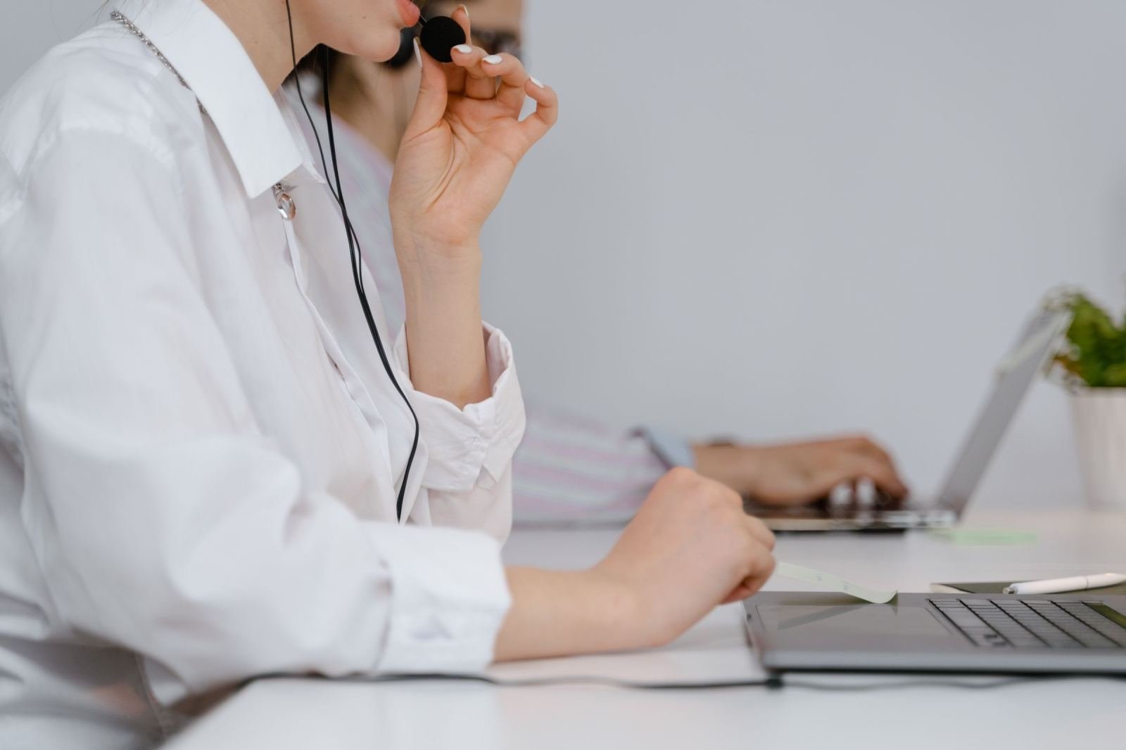 A person wearing a headset sits at a white desk with a laptop