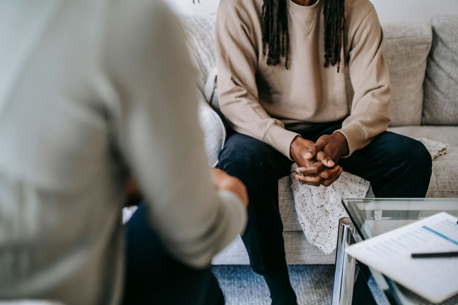 A person with dreadlocks sits on a sofa while speaking with a clinician