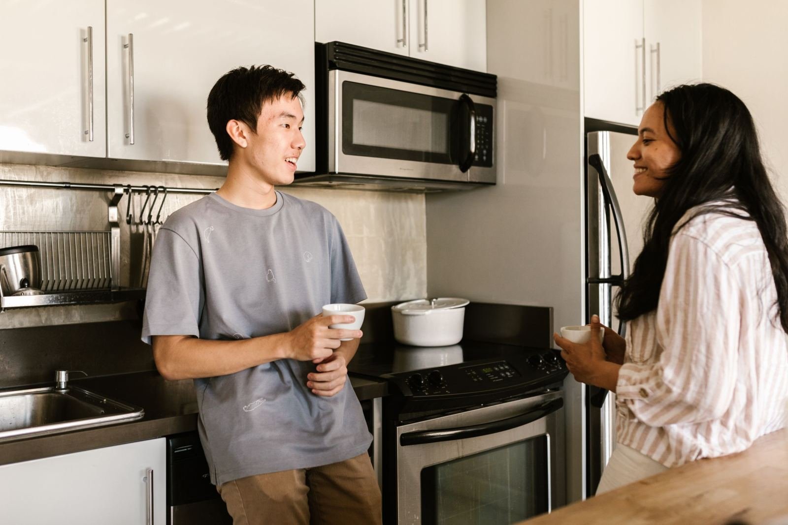 In a modern kitchen, a man and woman speak while holding cups.