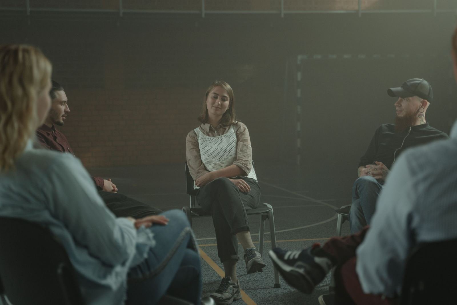 Four people sit in a circle of chairs in a dim room for a group discussion