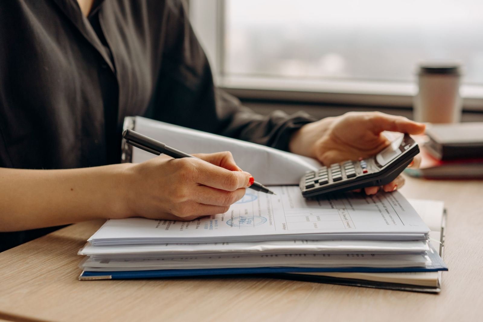 A person using a calculator and pen to review a stack of financial documents