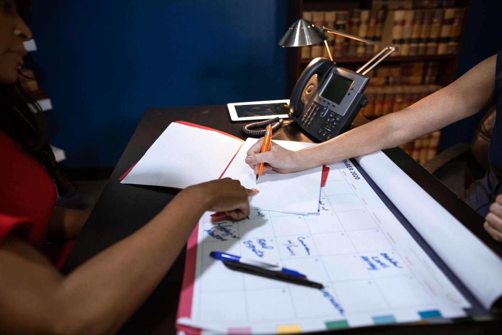 Two people review a weekly calendar and take notes at a desk