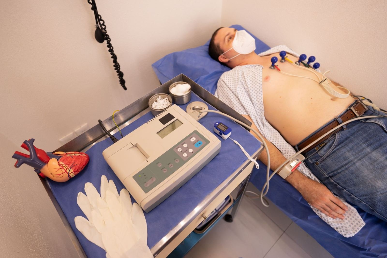 A man lies on an exam table with heart monitoring electrodes on his chest